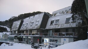 A multi-story building with a snow-covered roof and a ski lift in front. - Altitude Apartments (Falls Creek)