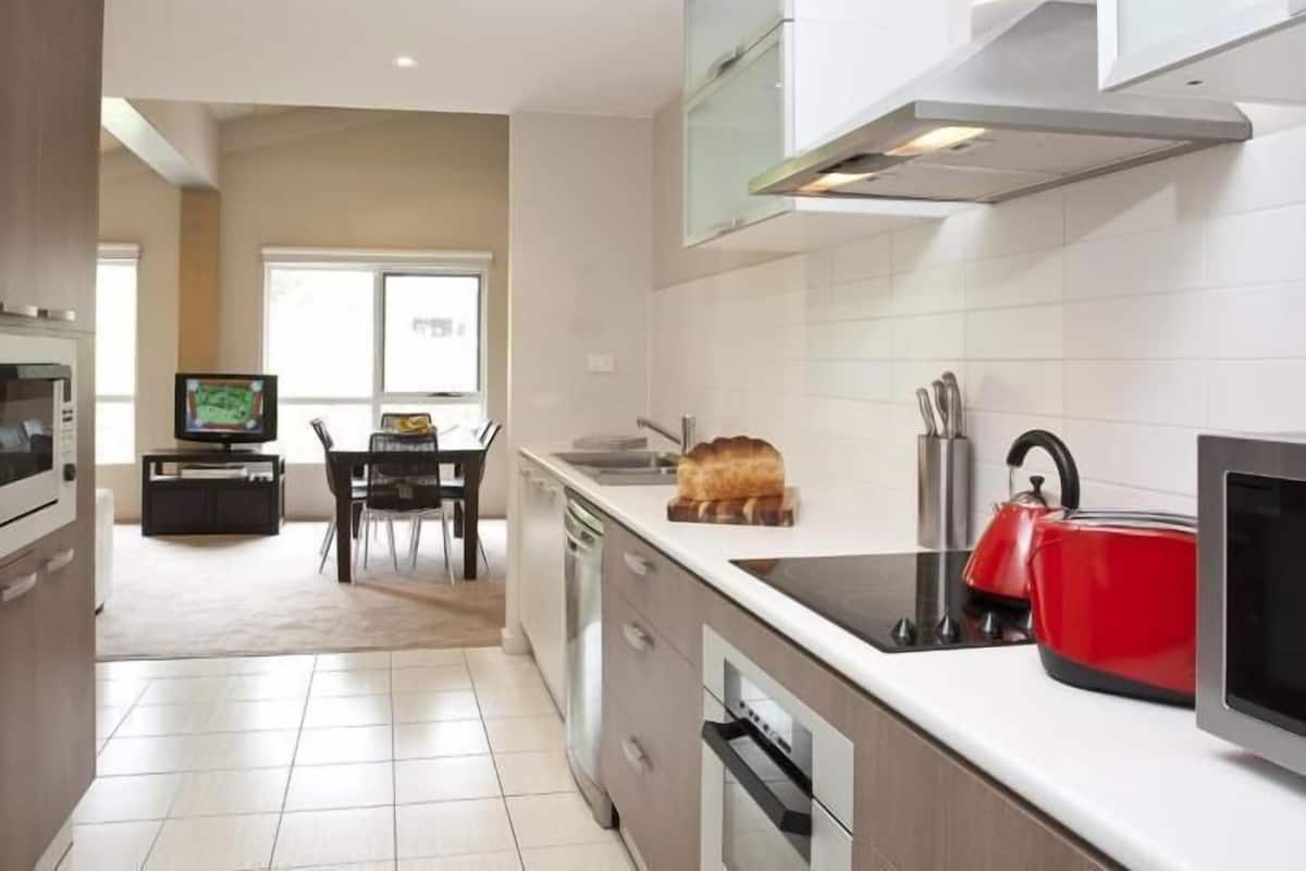 A modern kitchen with white cabinets, a red kettle, and a dining area with a TV.