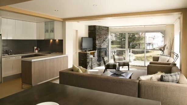 A modern kitchen with a stone accent wall, a flat-screen TV, and a fireplace. - Altitude Apartments (Falls Creek)