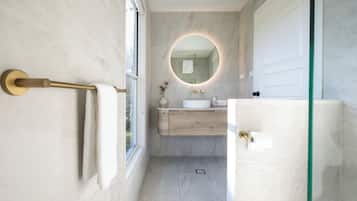 Een moderne badkamer met een marmeren wand, een ronde spiegel, een houten wastafelmeubel en een douchecabine van glas.