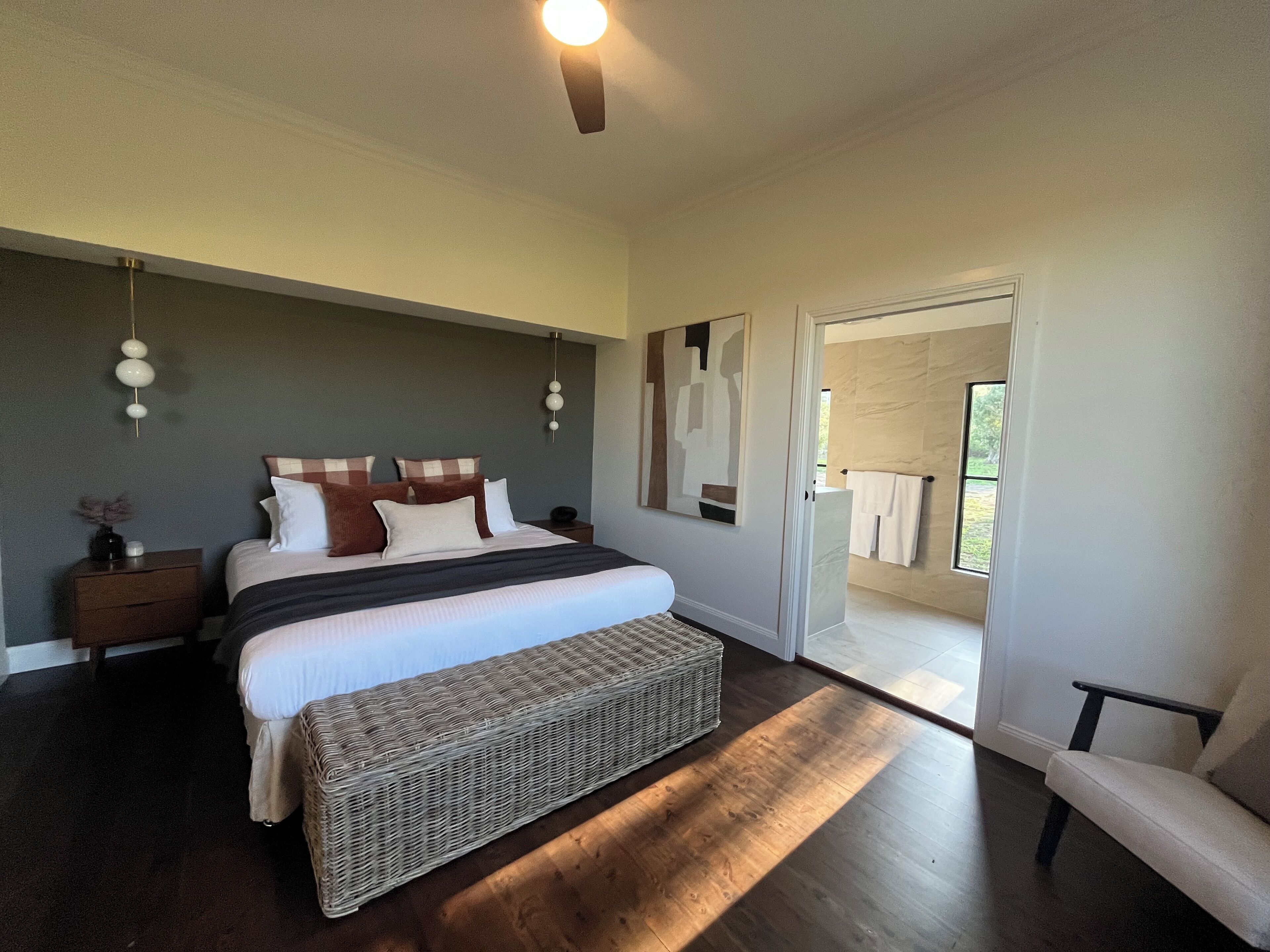 A modern bedroom with a large bed, a bedside table, a bench, and a view of the outdoors through a door.