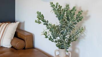 Ein braunes Ledersofa mit einem weißen Kissen, ein kleiner runder Tisch mit einer Vase mit Grünpflanzen und ein runder Spiegel an der Wand.