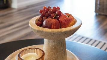 Une table à manger avec un panier de fruits contenant des raisins et des pommes, une bougie et une cheminée en arrière-plan.