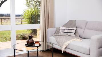 A living room with a grey sofa, a glass coffee table, and a view of a garden through a large window.
