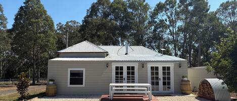 A single-story house with a metal roof, a front porch with a bench, and a small garden area.
