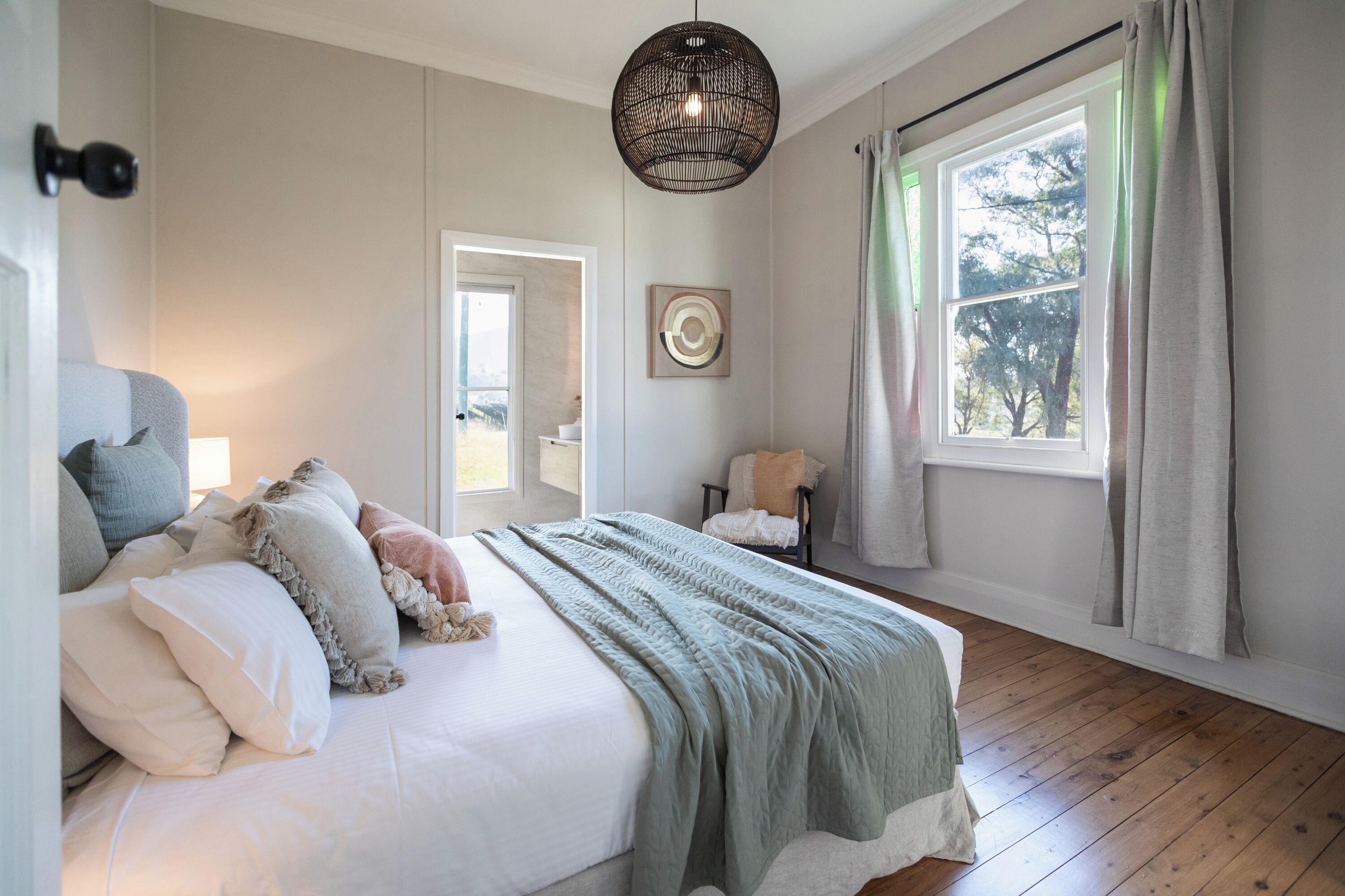 Ein Schlafzimmer mit einem großen Bett, einer Hängelampe, einem Fenster mit Vorhängen und einer Tür zu einem anderen Raum.