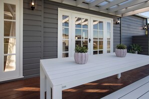 A covered patio with a white bench, two potted plants, and a white door with glass panels. - Pokolbin Farm Stay (Pokolbin)