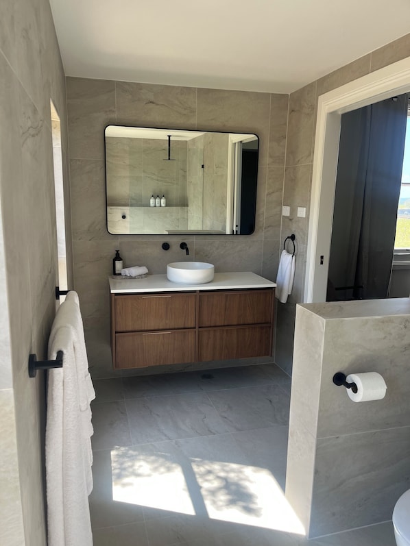 A modern bathroom with a large mirror, a round sink, wooden cabinets, and a toilet. - Pokolbin Farm Stay (Pokolbin)