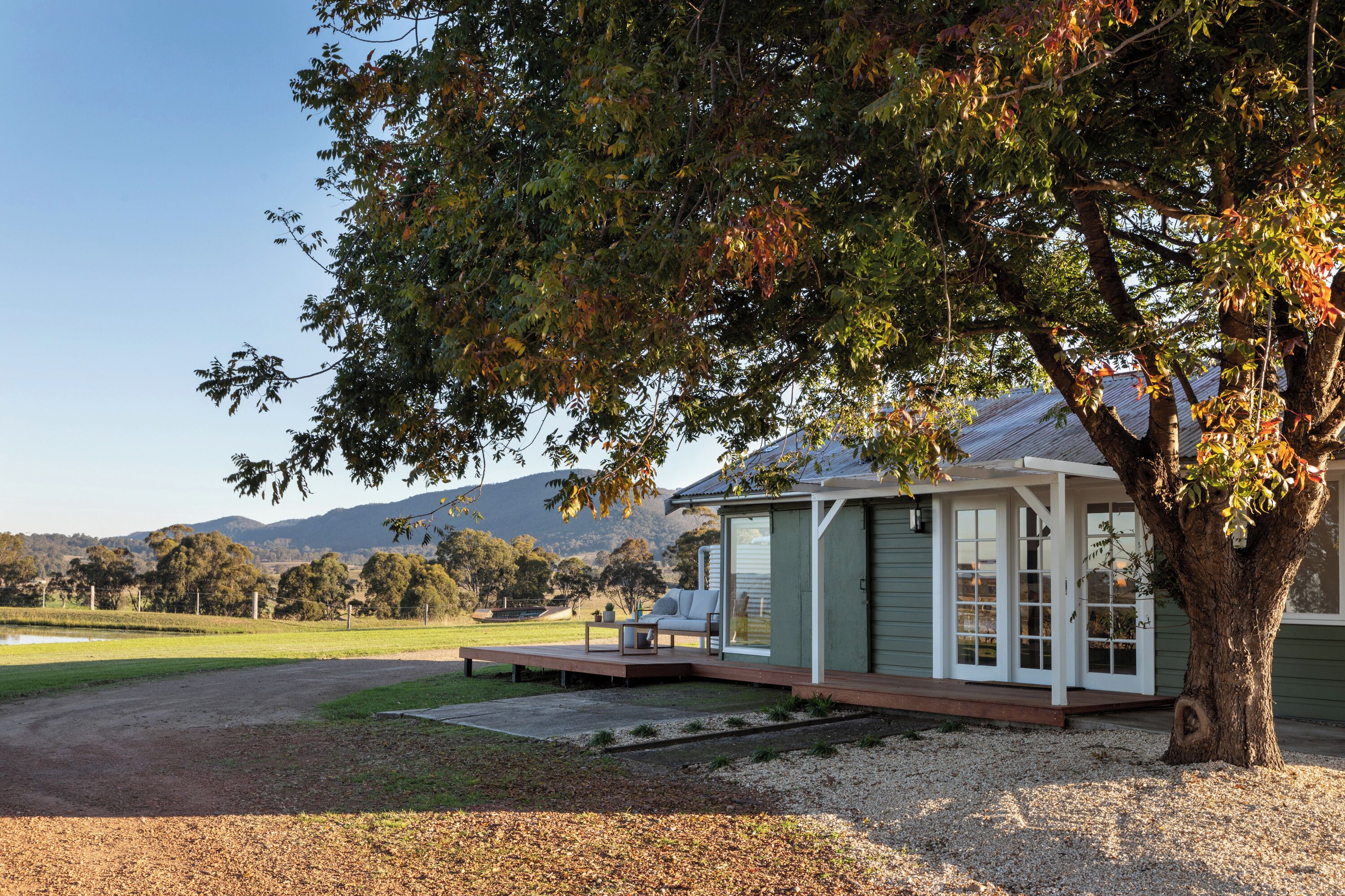 Una casa con terraza, un árbol grande y vistas al campo.