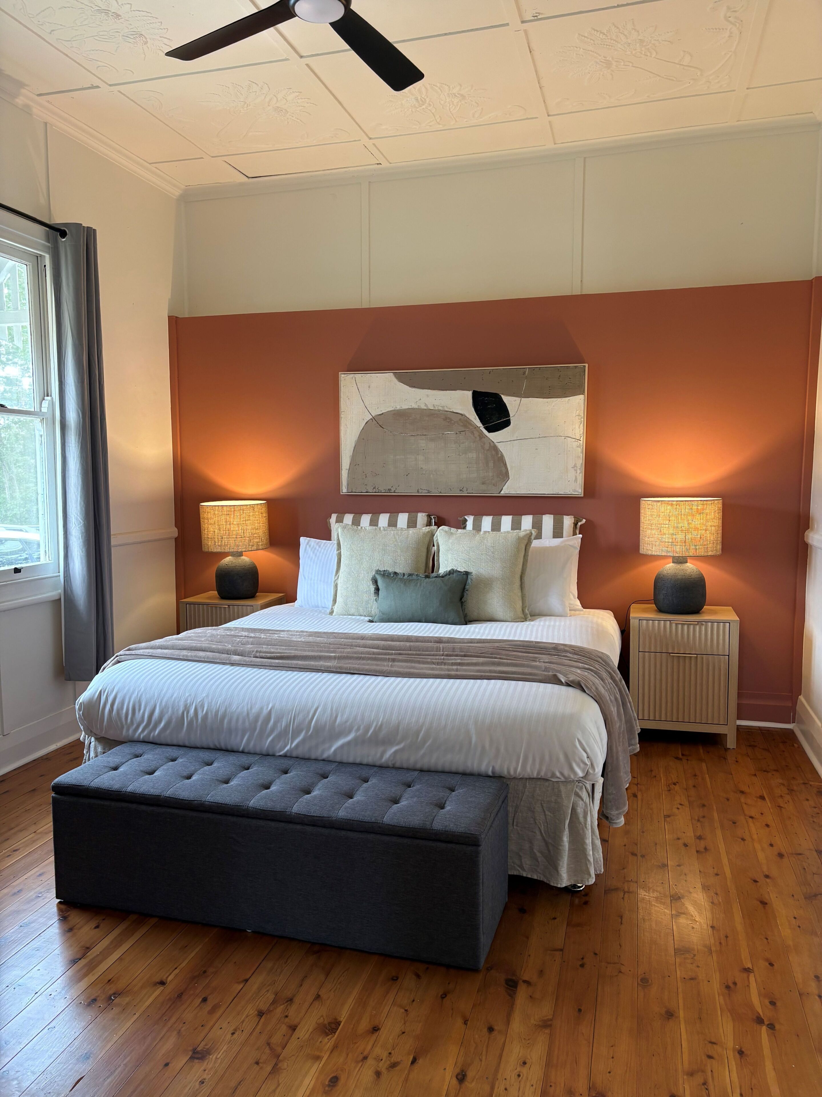 A bedroom with a bed, two bedside tables, a ceiling fan, and a window with curtains.
