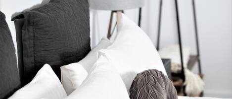 A bedroom with a bed, pillows, a hanging light fixture, a plant, and a clothing rack.