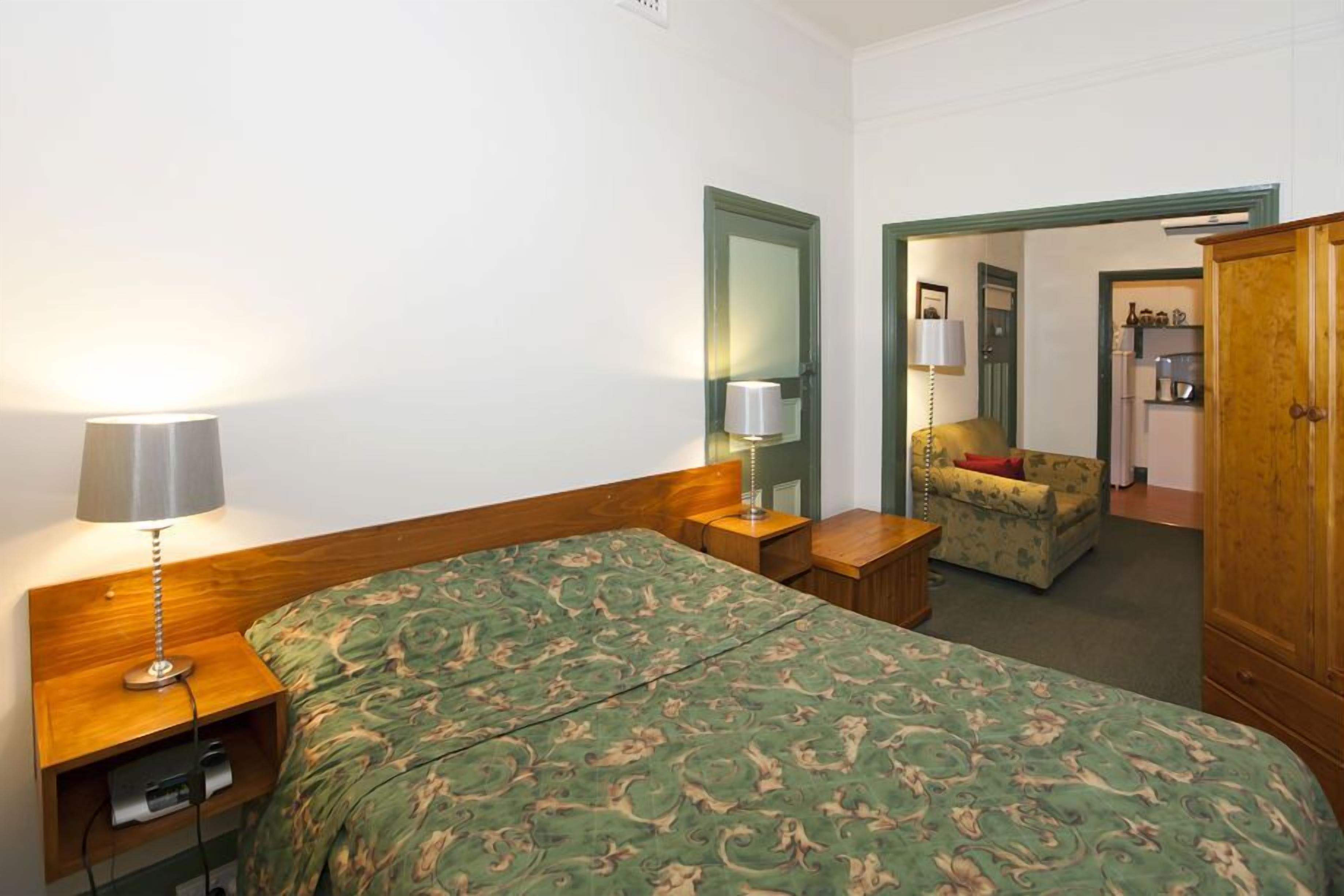 A hotel room with a large bed, bedside lamps, a small table, a chair, and a wardrobe.