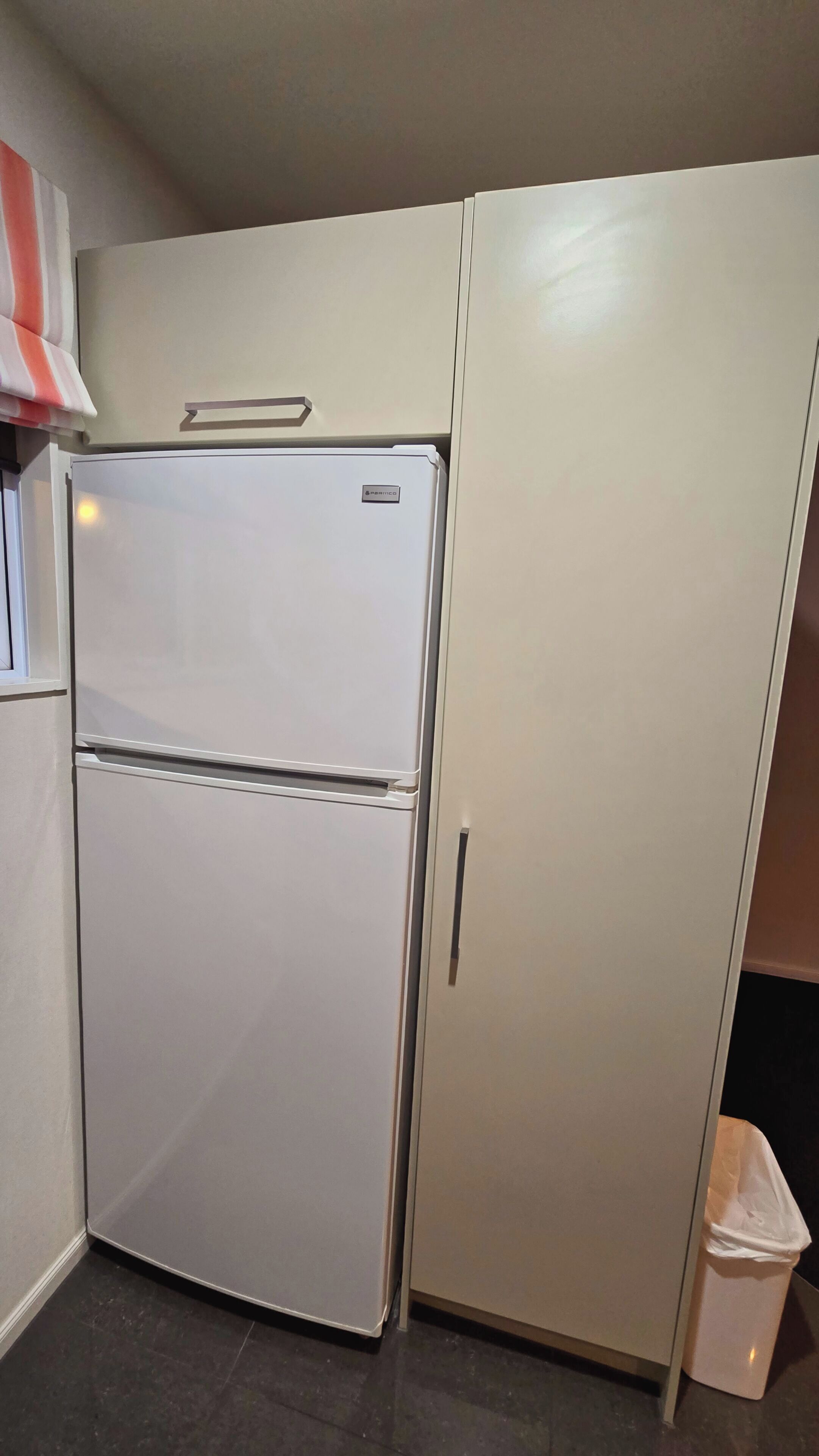 Una cocina compacta con un refrigerador blanco, un bote de basura pequeño y un armario.