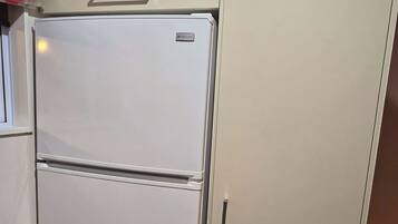 Una cocina compacta con un refrigerador blanco, un bote de basura pequeño y un armario.