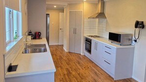 A modern kitchen with white cabinetry, a central island, and a microwave. - Carramar Motor Inn (Palmerston North)