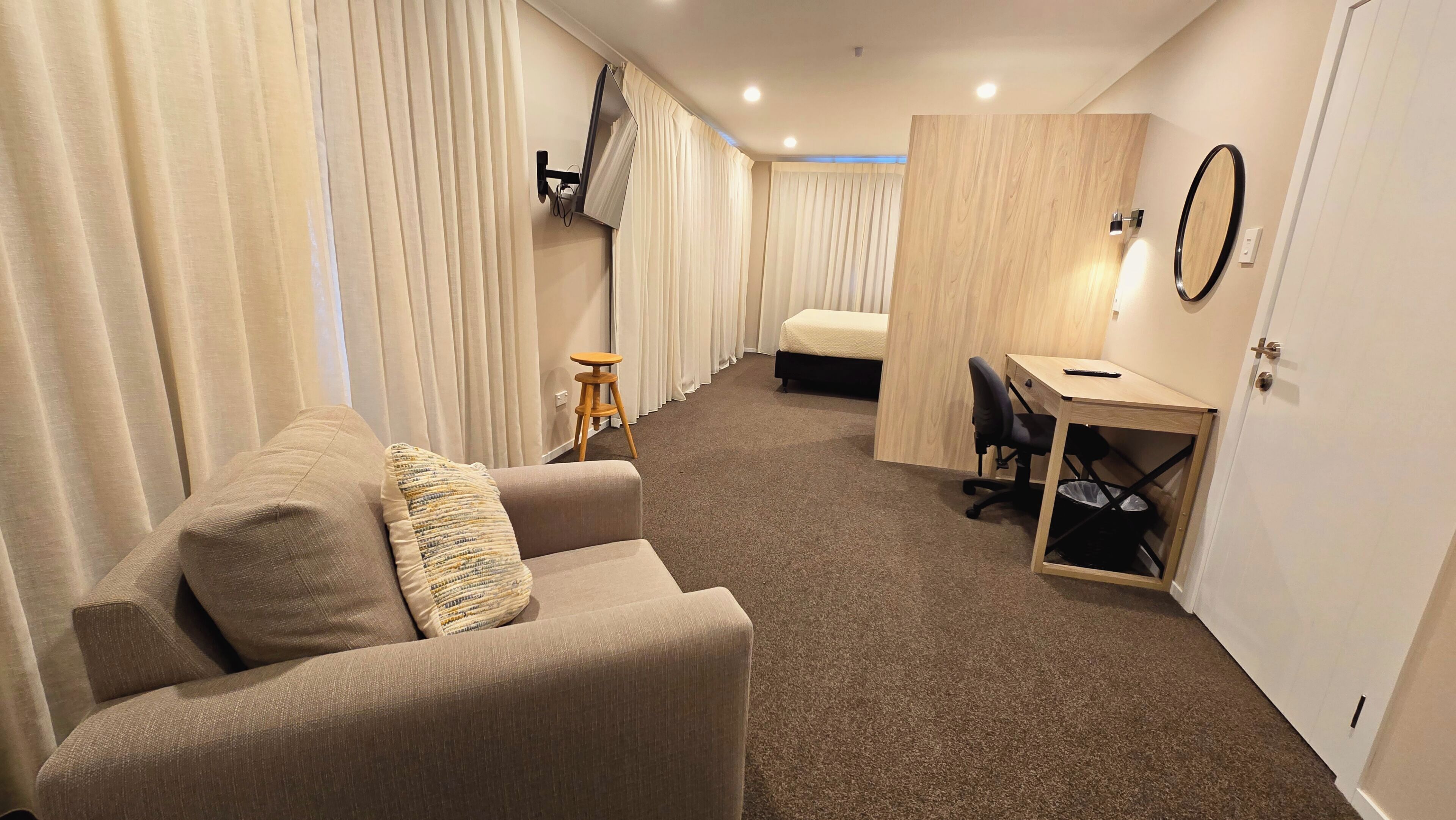 Habitación de hotel compacta con sofá, escritorio pequeño, una silla y una cama.