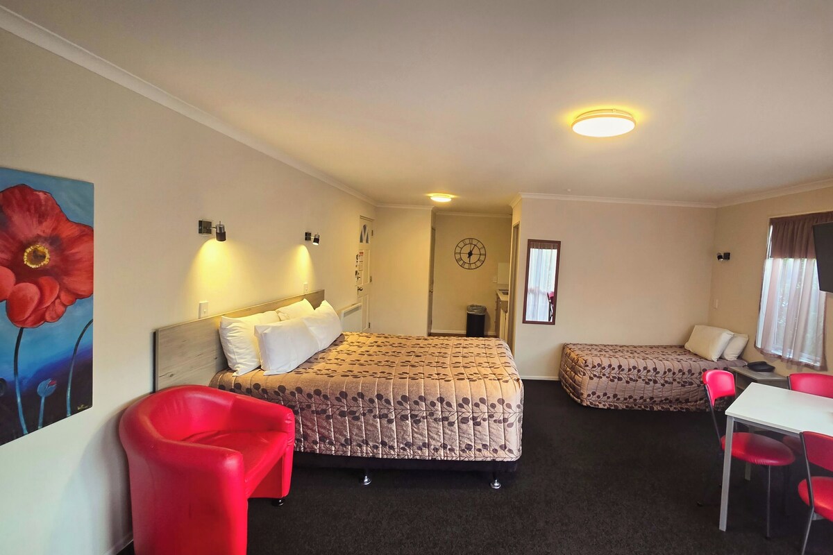 A hotel room with two beds, a desk with a chair, a TV, and a painting on the wall.