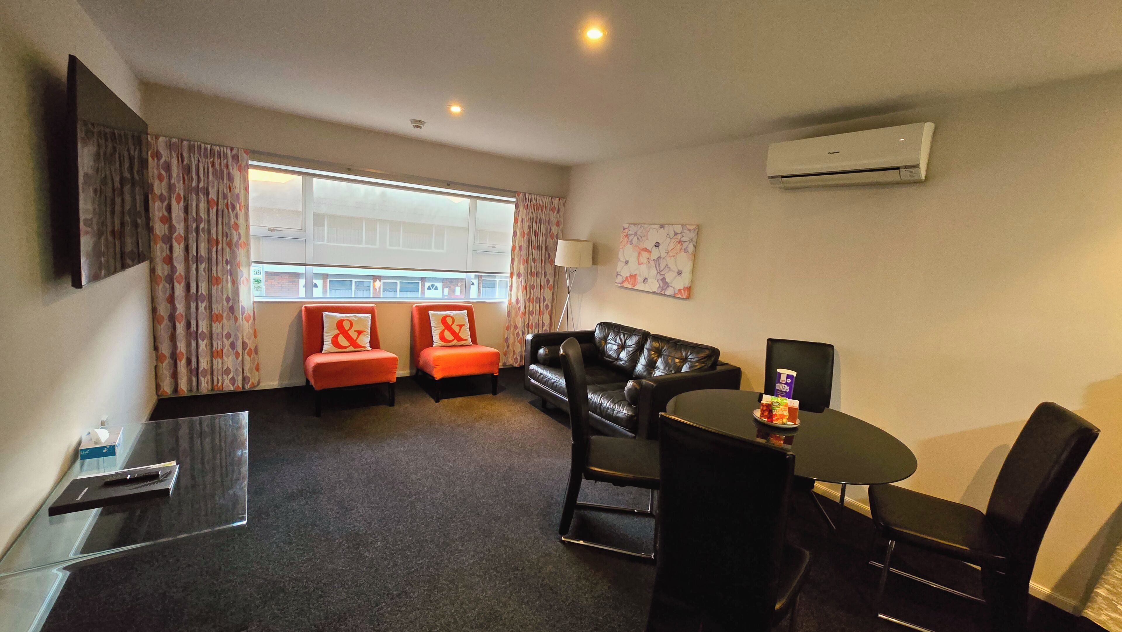 A hotel room with a sofa, two armchairs, a coffee table, a TV, and an air conditioner.