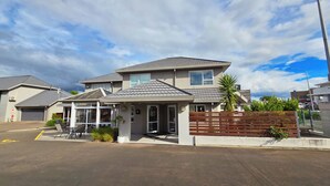 A two-story residential building with a garage, a covered patio, and a small garden area with a wooden fence and plants. - Carramar Motor Inn (Palmerston North)