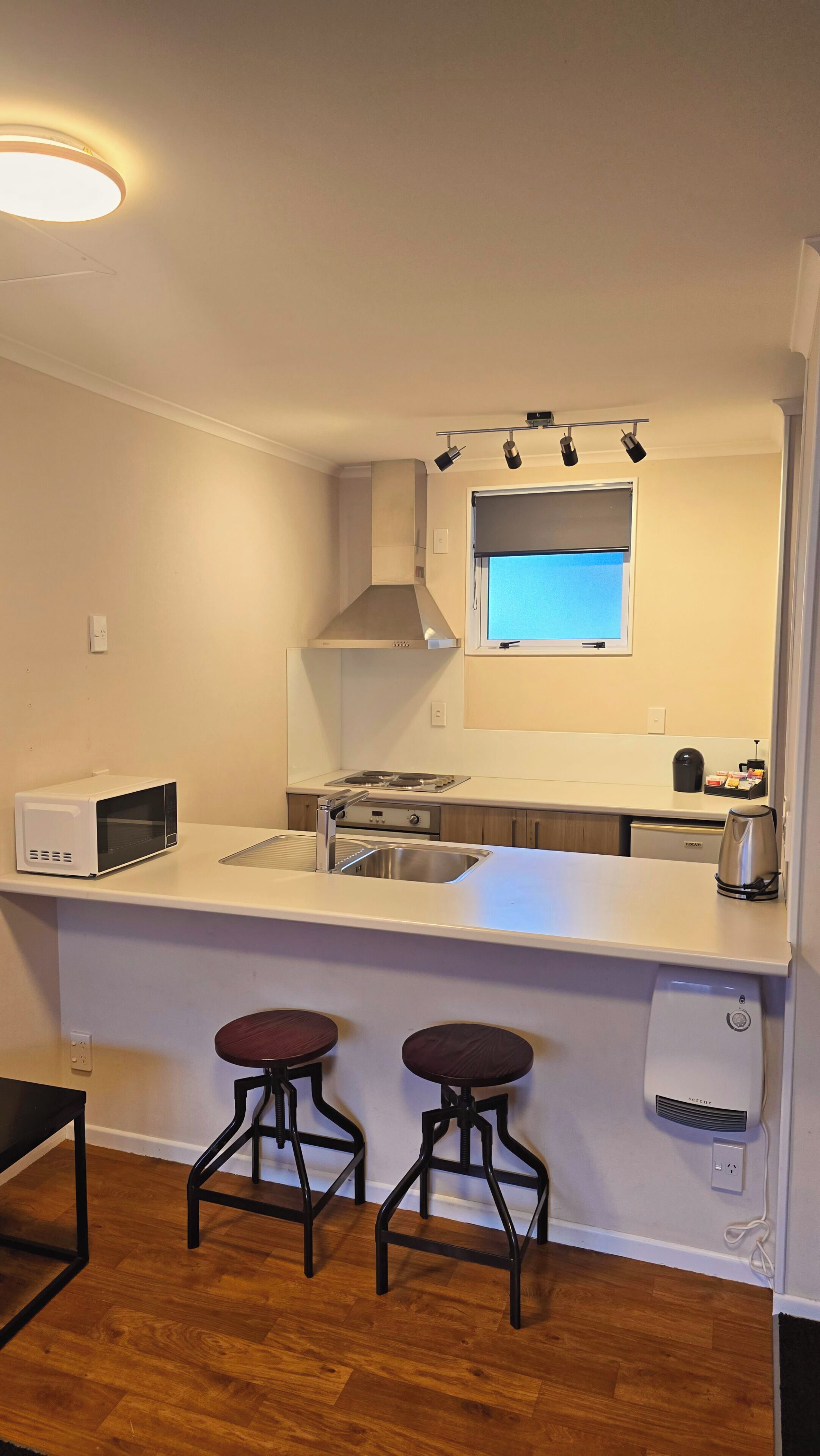 A compact kitchen with a microwave, stove, sink, and two stools.