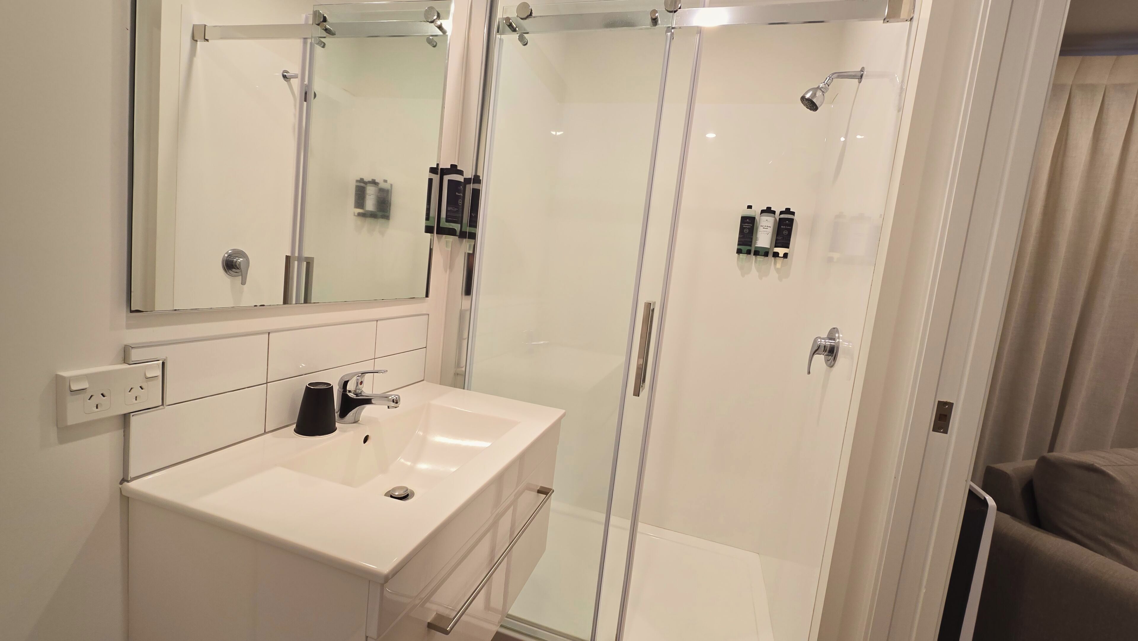 A modern bathroom with a white sink, a glass-enclosed shower, and a large mirror.