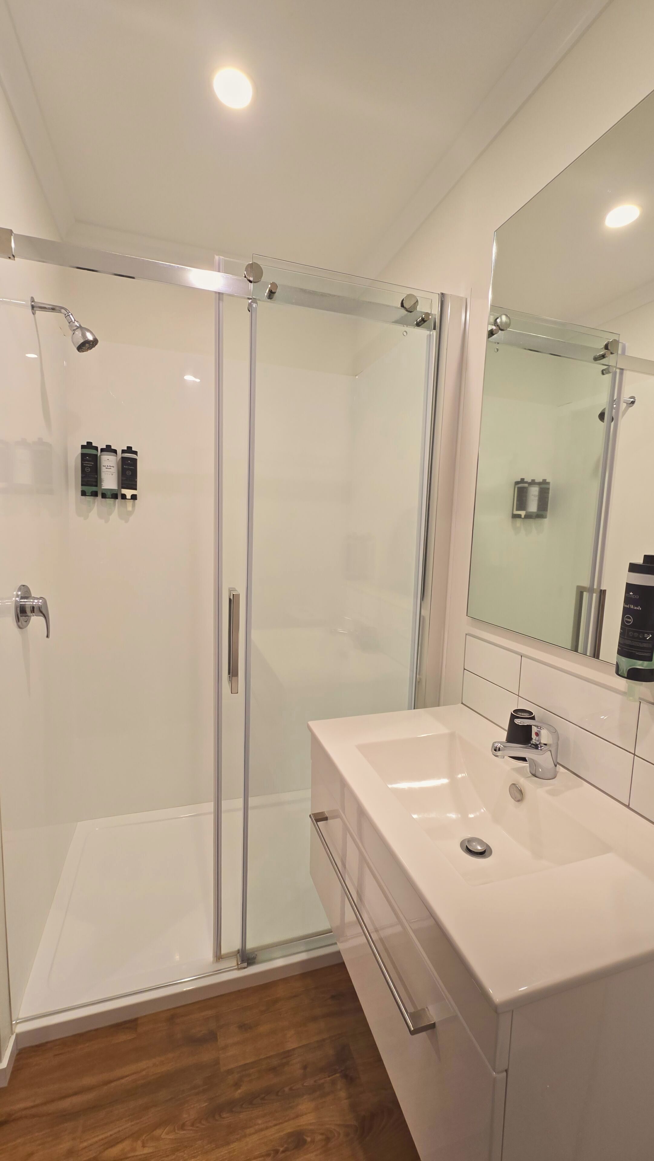 Un baño moderno con ducha envuelta en vidrio, un lavabo blanco y un espejo grande.