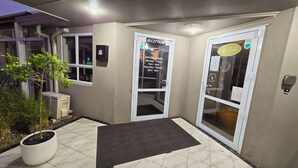 A reception area with a reception desk, a sign indicating office hours, and a door labeled "Café Zest." - Carramar Motor Inn (Palmerston North)