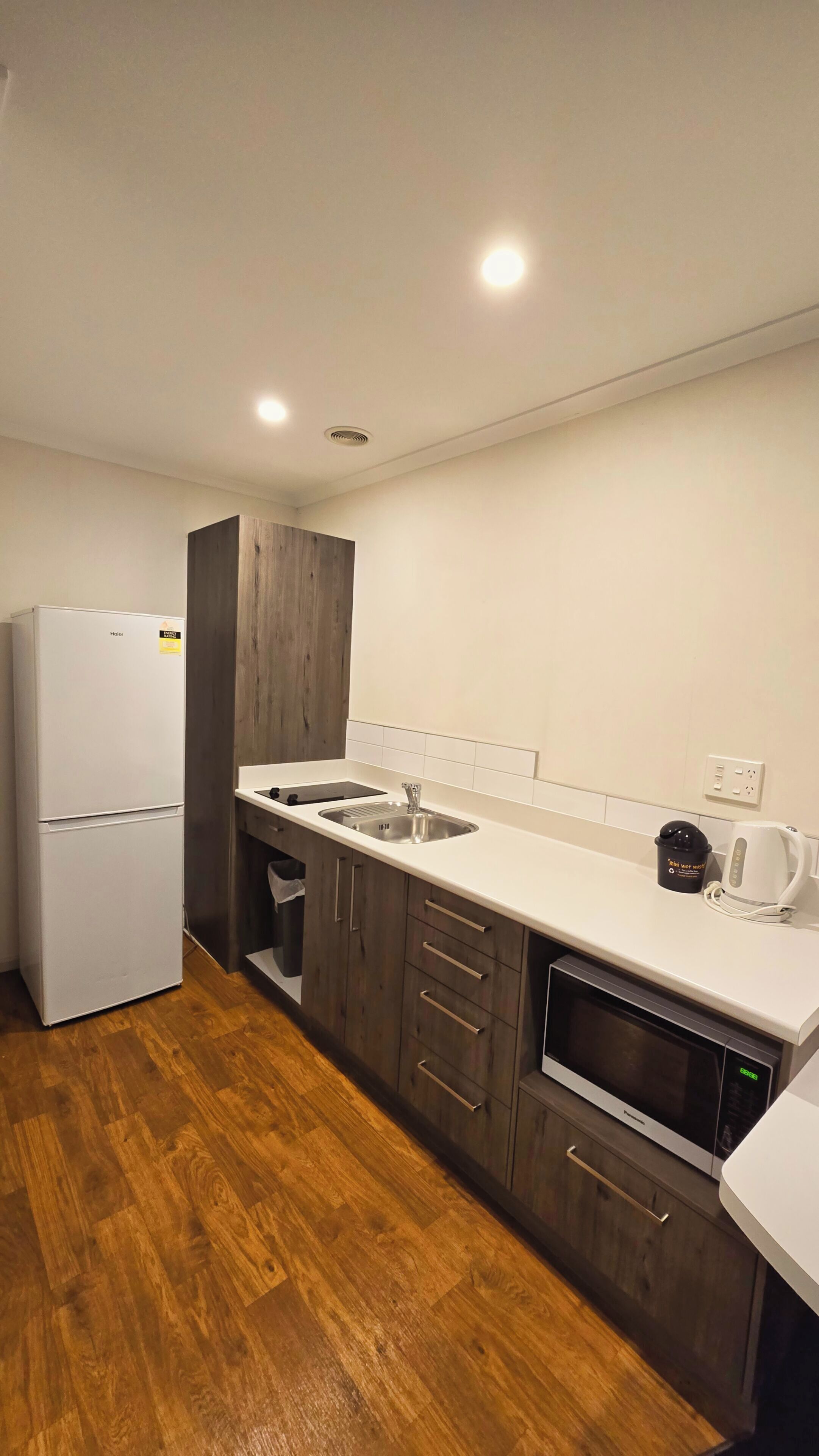 A modern kitchen with a refrigerator, sink, microwave, and wooden cabinets.