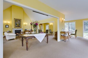 A spacious living room with a fireplace, a dining area with a table set for four, and a large window providing natural light. - Glen Isla House (Cowes)