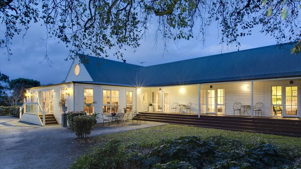 A two-story building with a covered porch, outdoor seating, and a well-lit entrance. - Glen Isla House (Cowes)