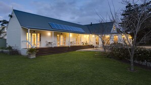 A house with a sloped roof, solar panels, a covered porch with outdoor seating, and a well-maintained lawn. - Glen Isla House (Cowes)