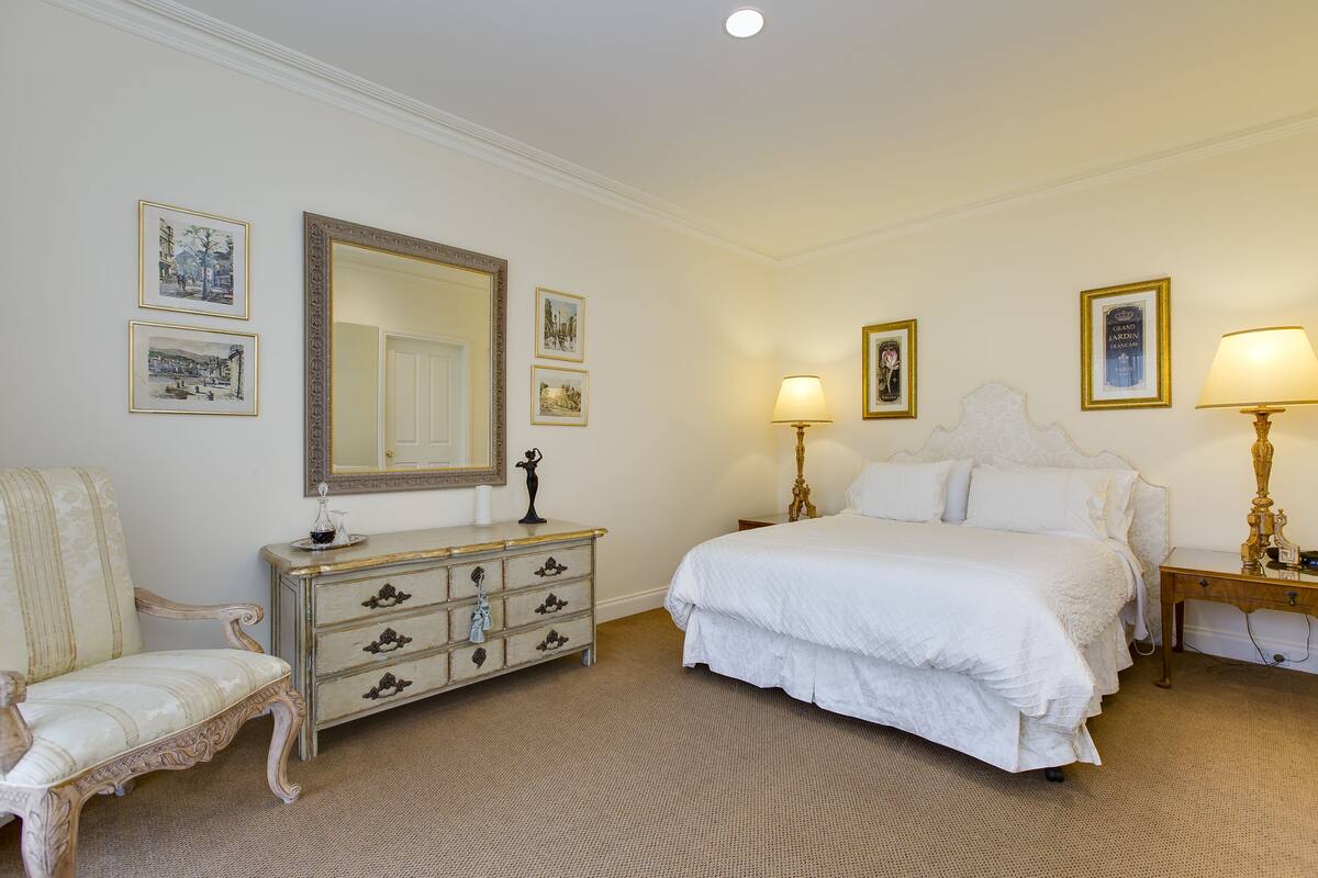 A bedroom with a large bed, a dresser, a chair, and a mirror.