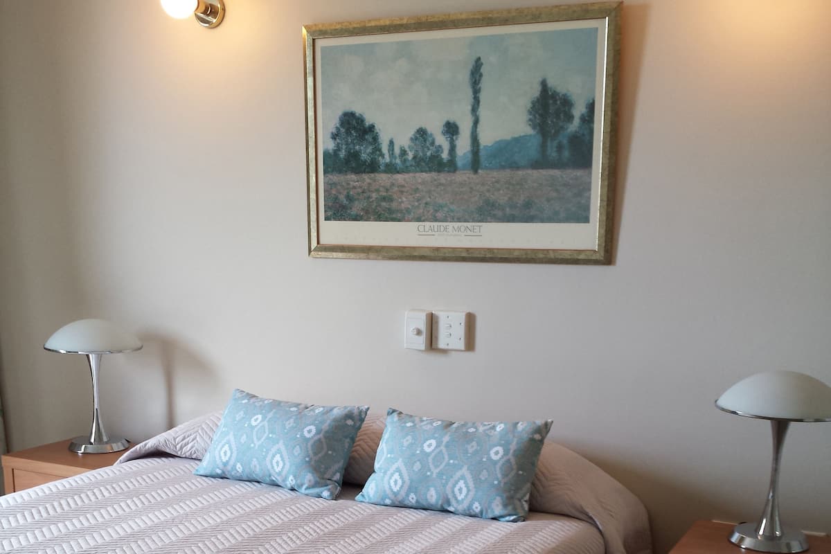 A neatly made bed with patterned pillows, a framed painting above it, and two bedside lamps on wooden nightstands.