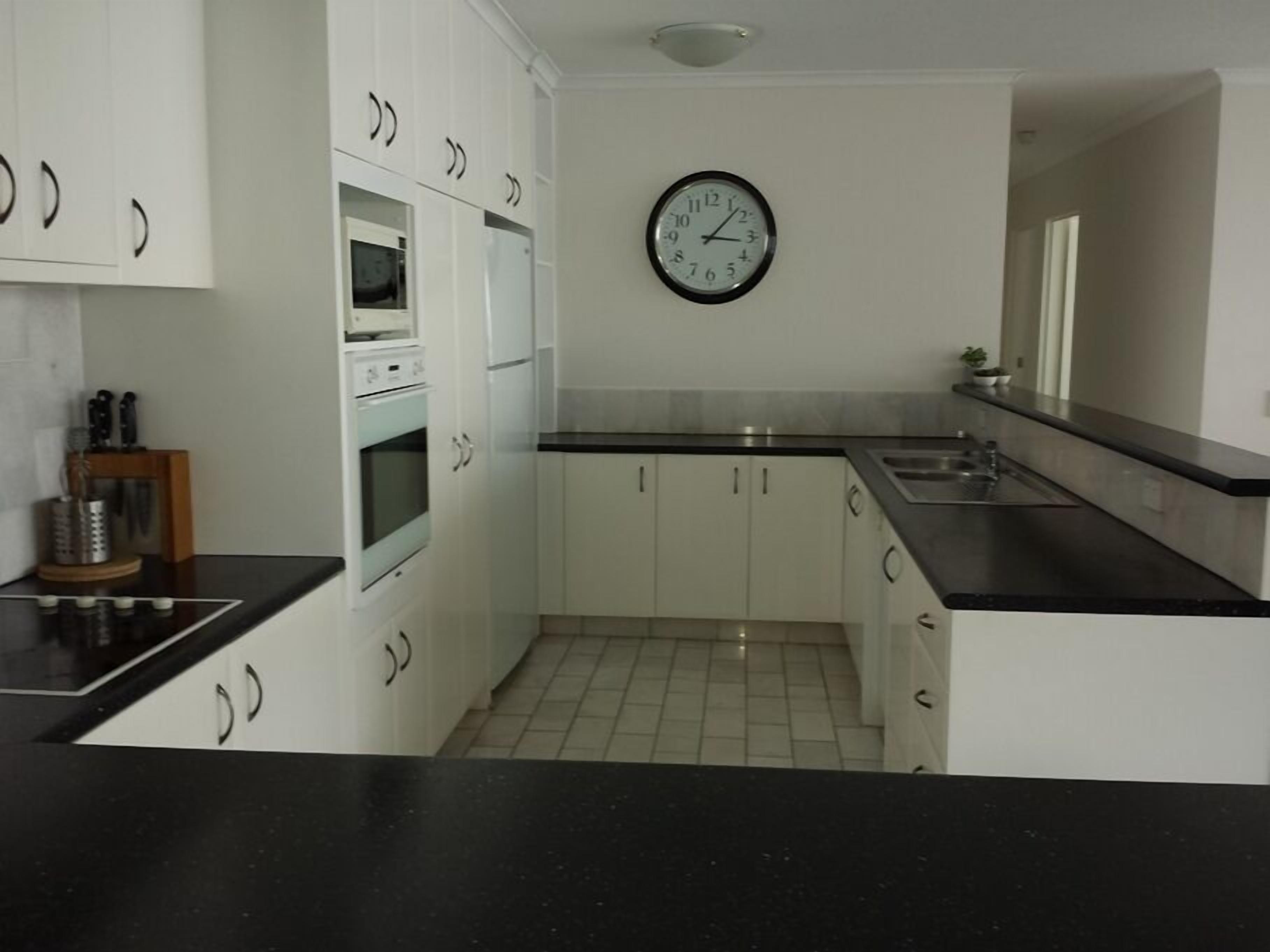 A modern kitchen with white cabinets, a black countertop, and a wall clock.