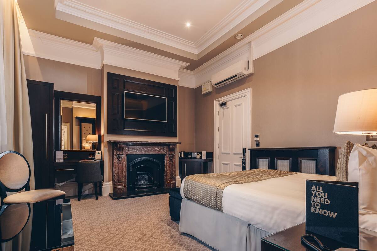 A hotel room with a bed, a desk, a chair, a fireplace, and a television.