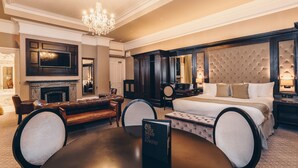 Ein luxuriöses Hotelzimmer mit einem großen Bett, einem Kamin, einem Esstisch und einer Kristallleuchter.