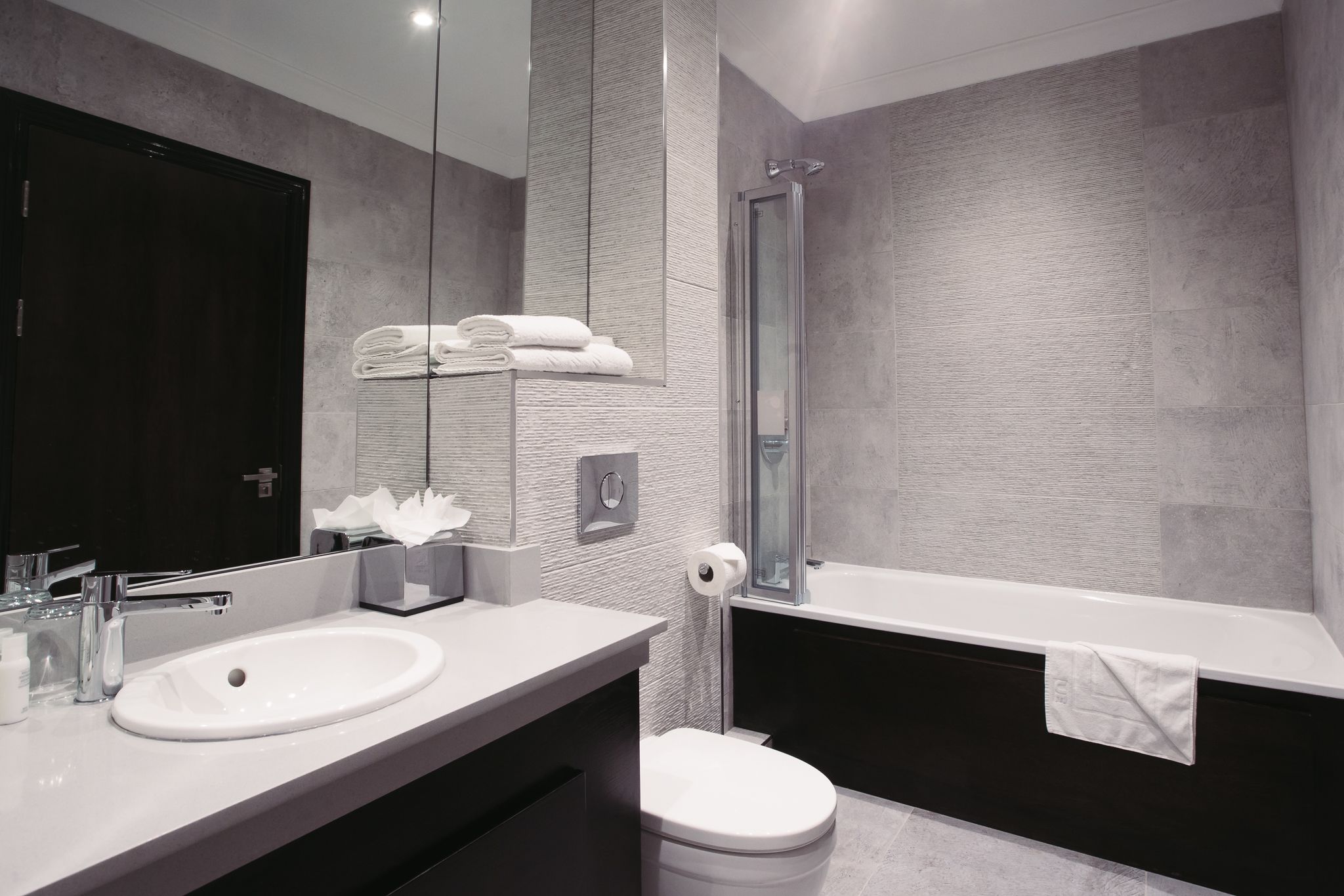 A modern bathroom with a double sink, a toilet, a bathtub, and a glass shower enclosure.