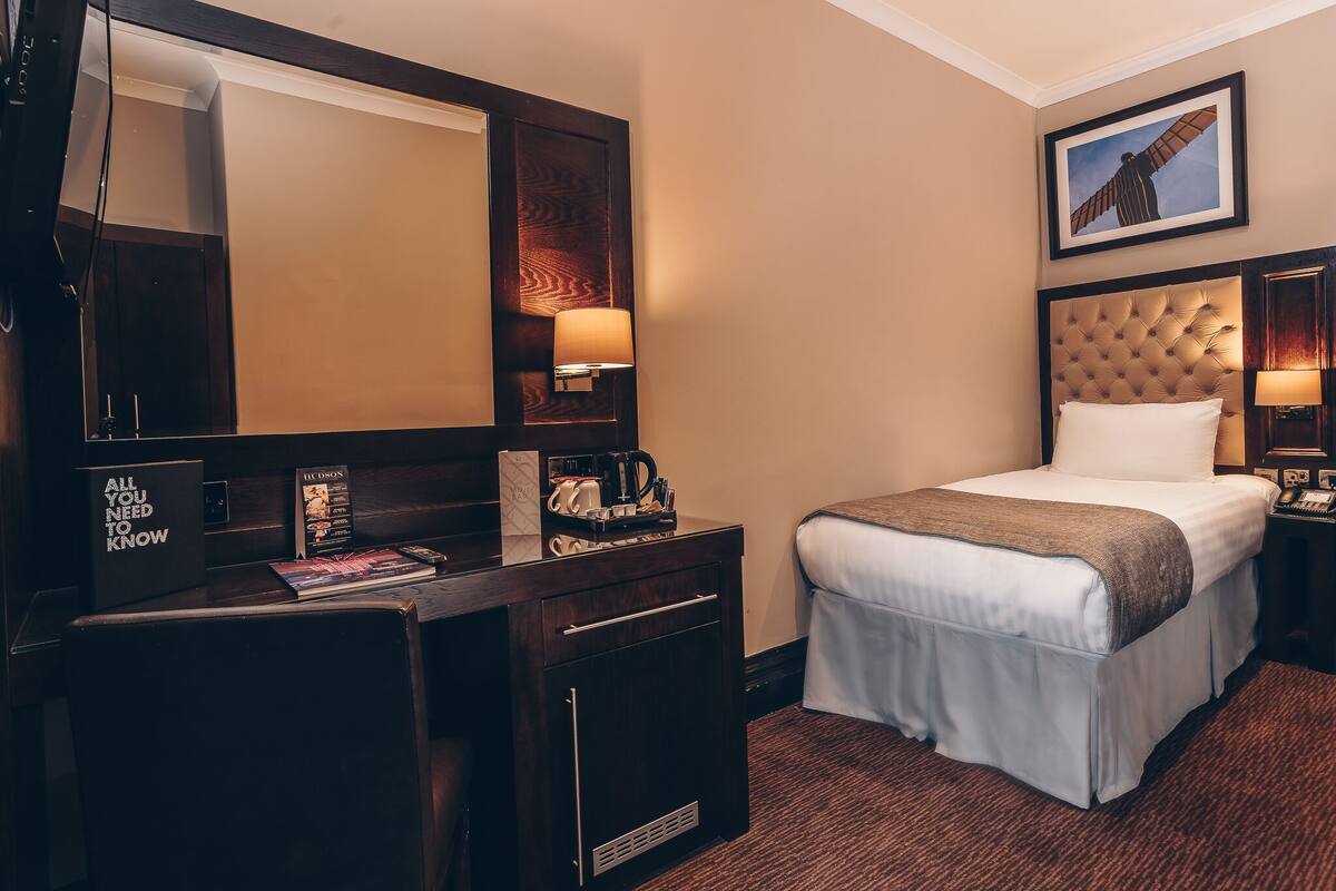A hotel room with a large bed, a desk with a mirror, a coffee machine, and a framed picture on the wall.