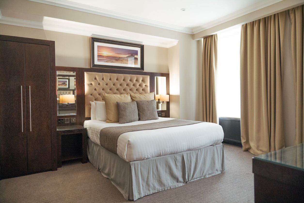 A hotel room with a large bed, a wooden wardrobe, a framed picture above the bed, and a window with curtains.