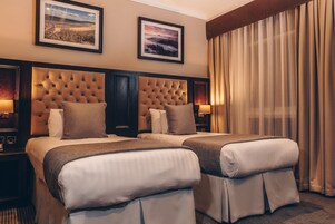 A hotel room with two beds, a large tufted headboard, and two framed pictures on the wall.
