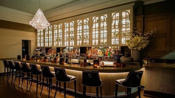 Eine Bar mit einer langen Theke, mehreren Hockern und einer großen Chandelier.