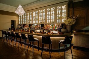 A bar with a long counter, multiple stools, and a large chandelier. - The County Hotel, Newcastle (Newcastle-upon-Tyne)