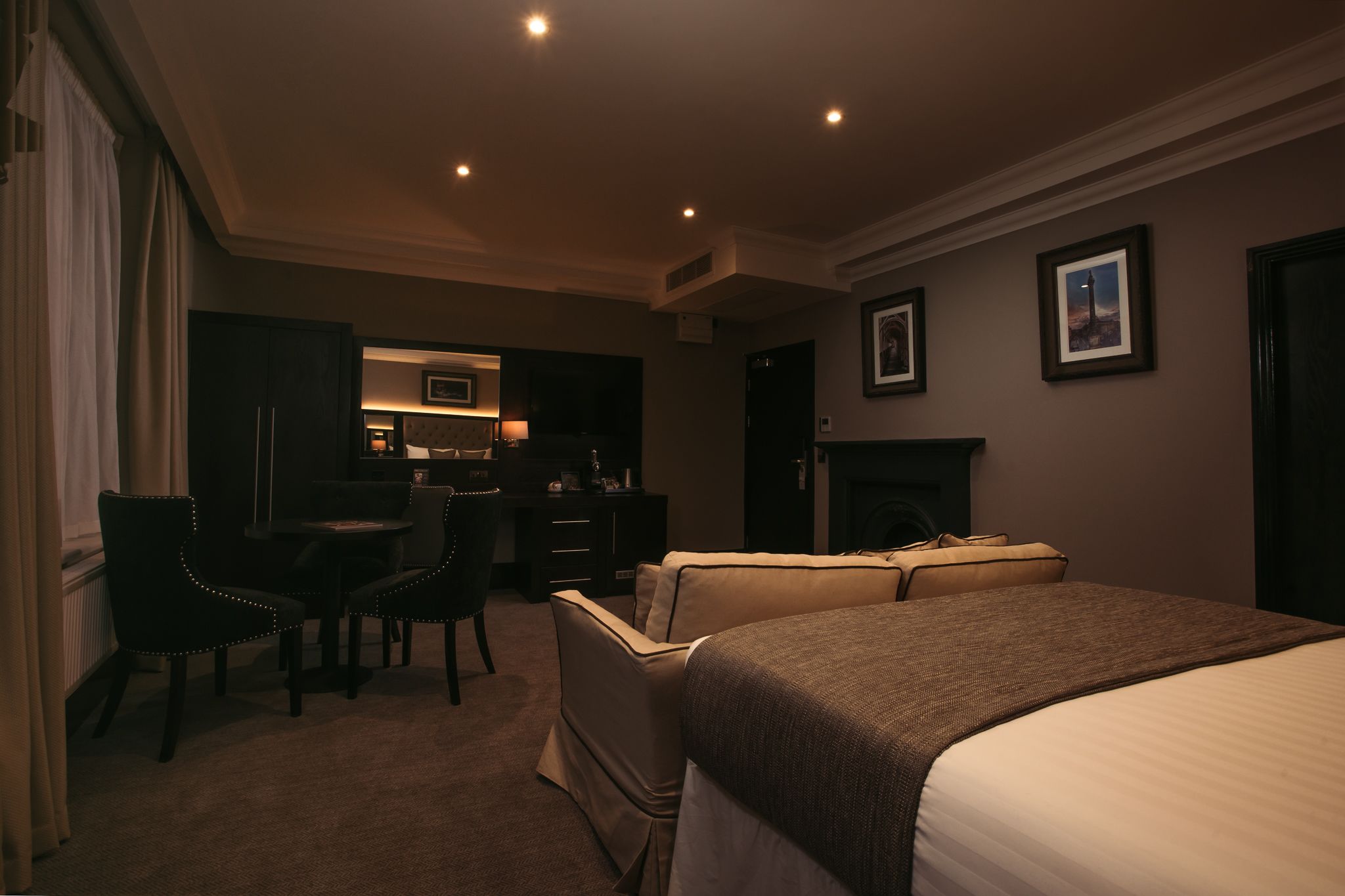 A hotel room with a bed, a desk, a chair, and a fireplace.