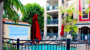 A pool area with lounge chairs and a red umbrella, surrounded by a fence. - Montego Sands Resort (Mermaid Beach)