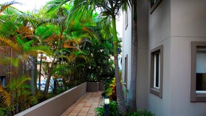 A corridor with a tiled floor, surrounded by lush greenery and palm trees, leading to a building with windows. - Montego Sands Resort (Mermaid Beach)
