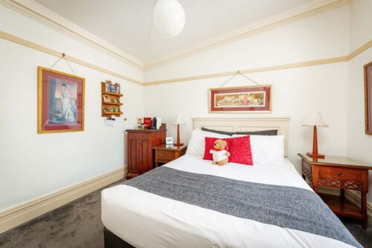 A neatly arranged bedroom with a large bed, bedside tables, a dresser, and framed artwork on the walls.