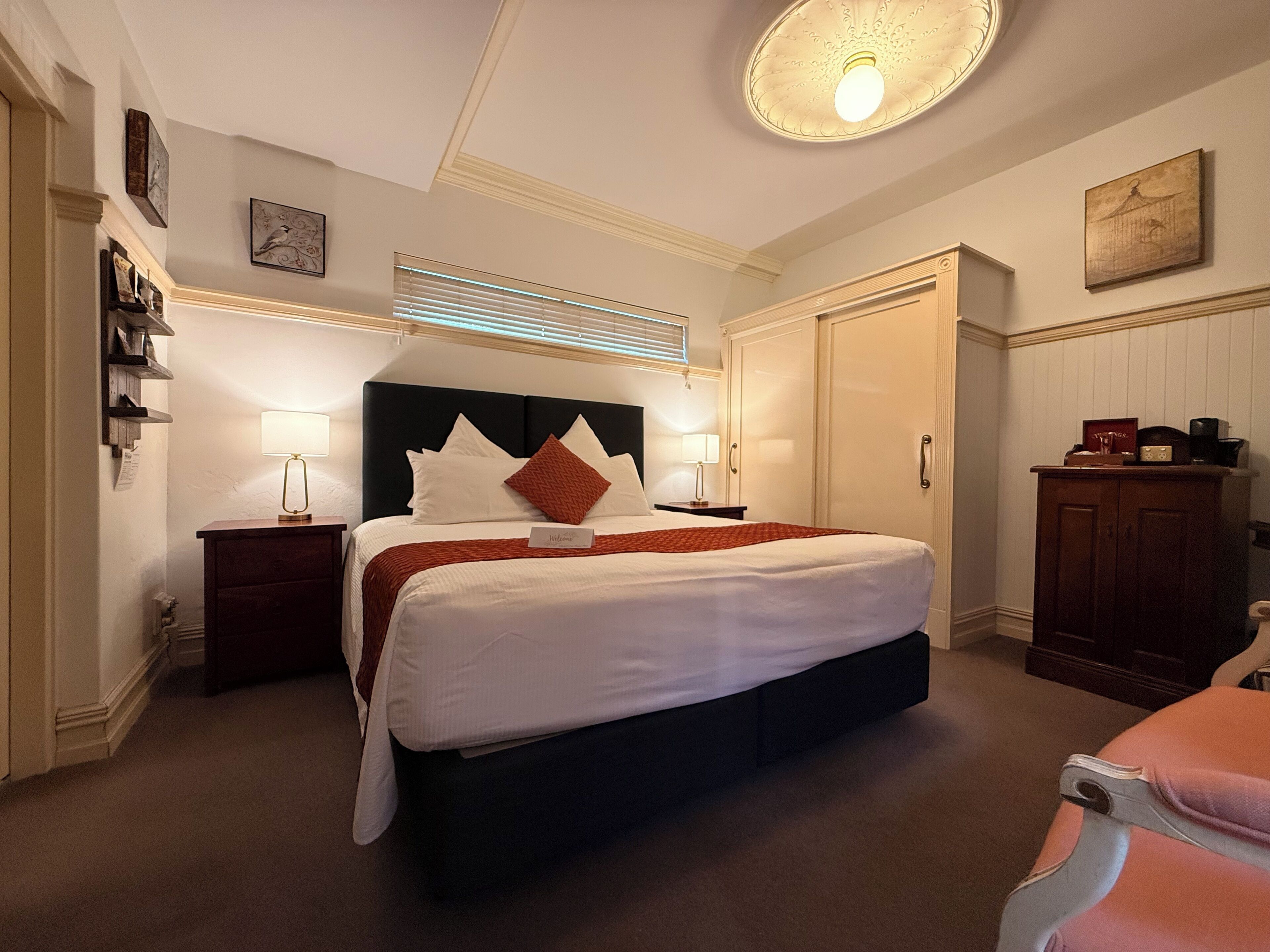 Une chambre d’hôtel avec un grand lit, des tables de chevet, une armoire et un luminaire au plafond.