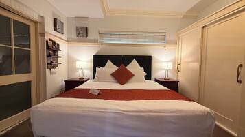 A neatly arranged hotel room with a large bed, two bedside tables with lamps, a window with blinds, and a door.