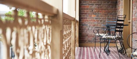 A balcony with a patterned floor, a brick wall, and two metal chairs.
