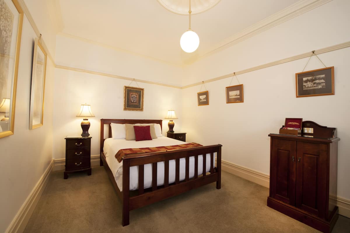 A neatly arranged bedroom with a wooden bed, bedside tables with lamps, framed pictures on the wall, and a cabinet.